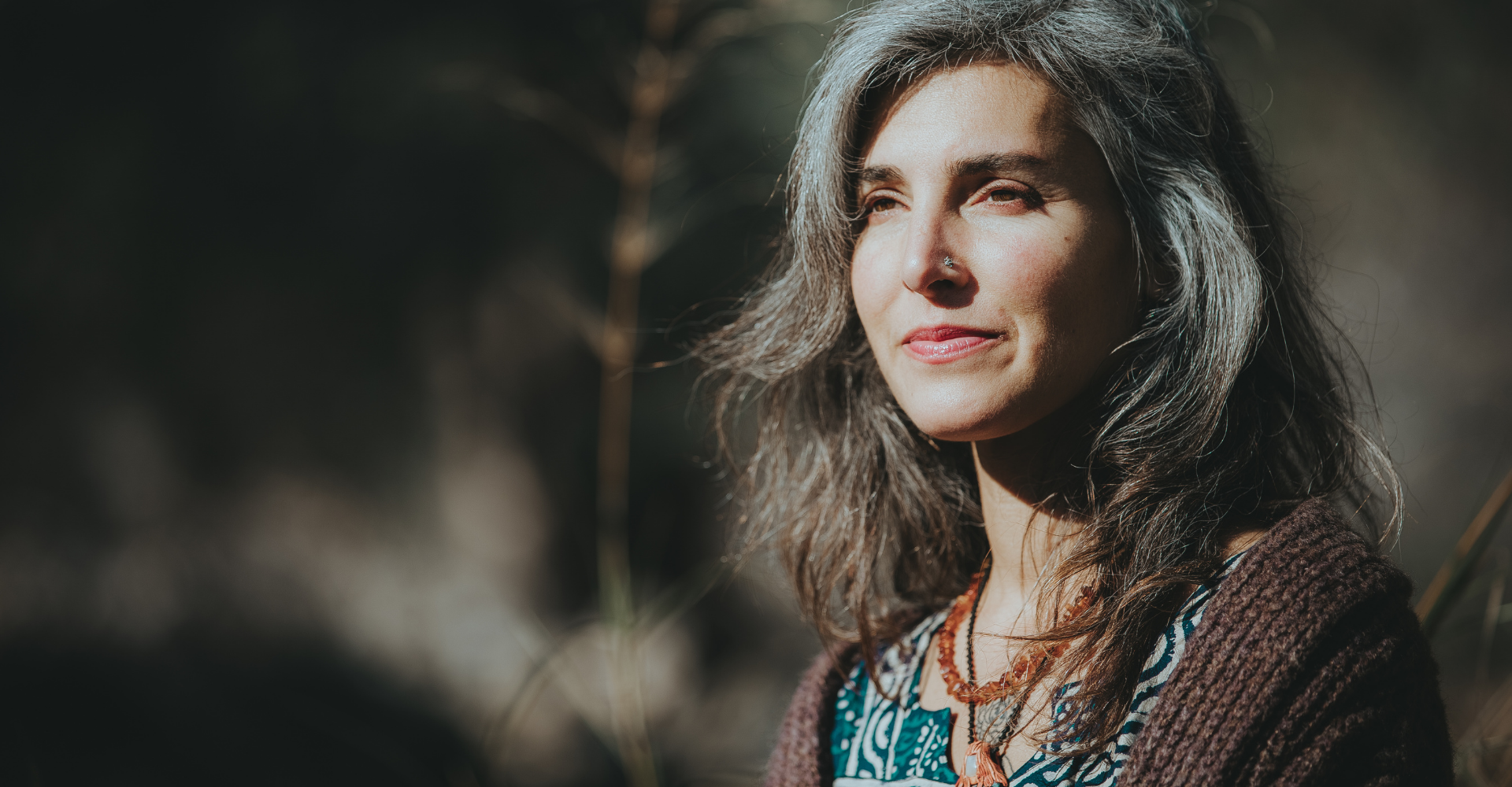 white woman with long gray hair and nose ring looks to the left of the frame
